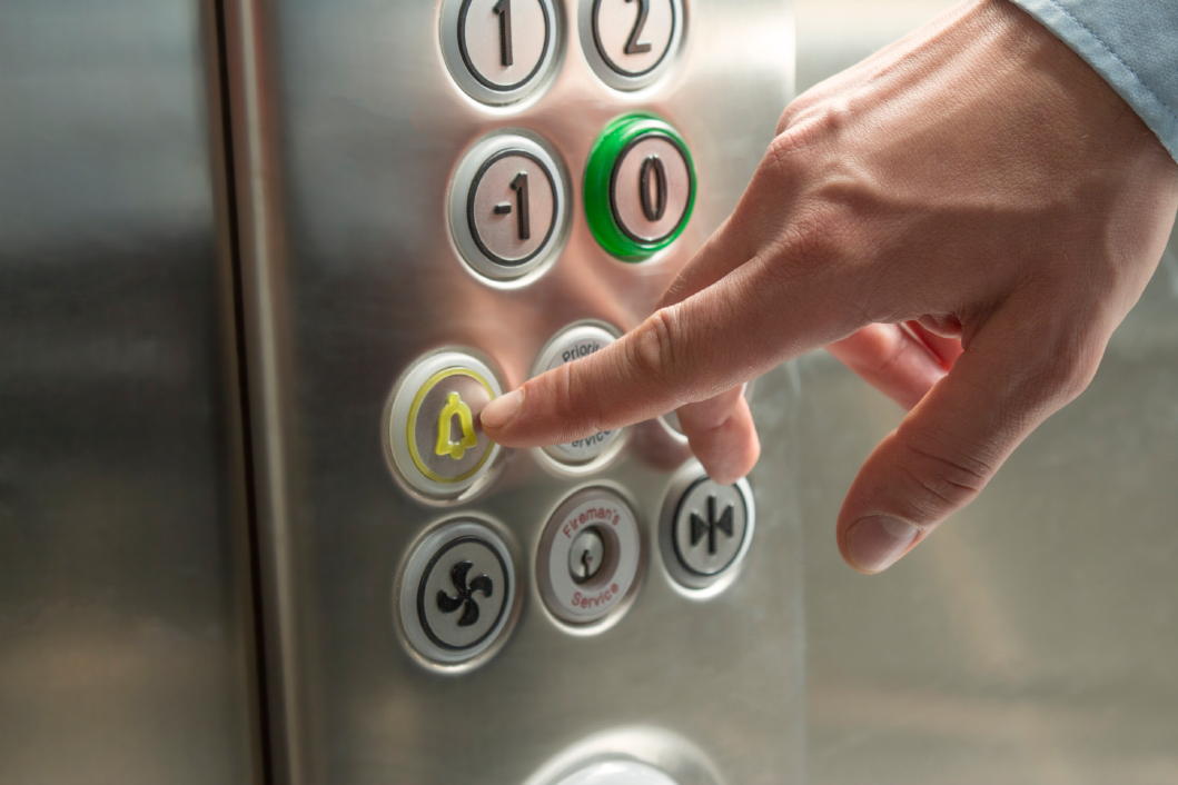 Elevator buttons with a hand about to touch the alarm bell